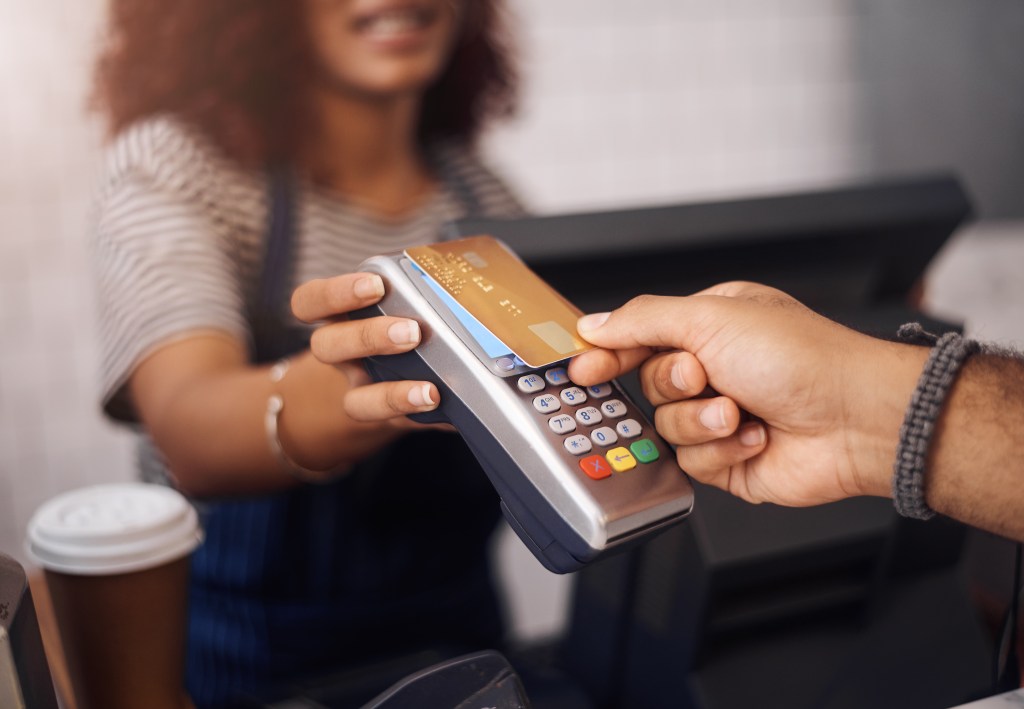 Customer making a contactless credit card payment at a coffee checkout using an NFC-enabled point-of-sale machine